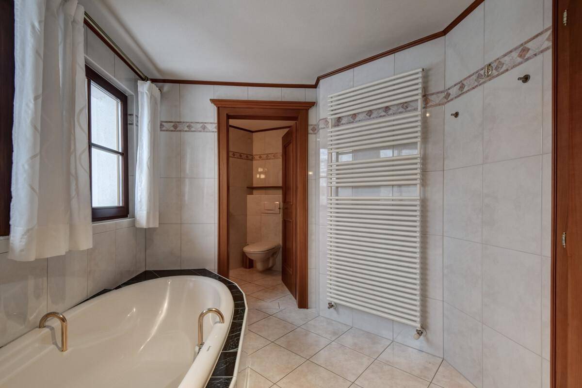 Badezimmer mit Badewanne, beheiztem Handtuchhalter und Zugang zu einer separaten Toilette.
