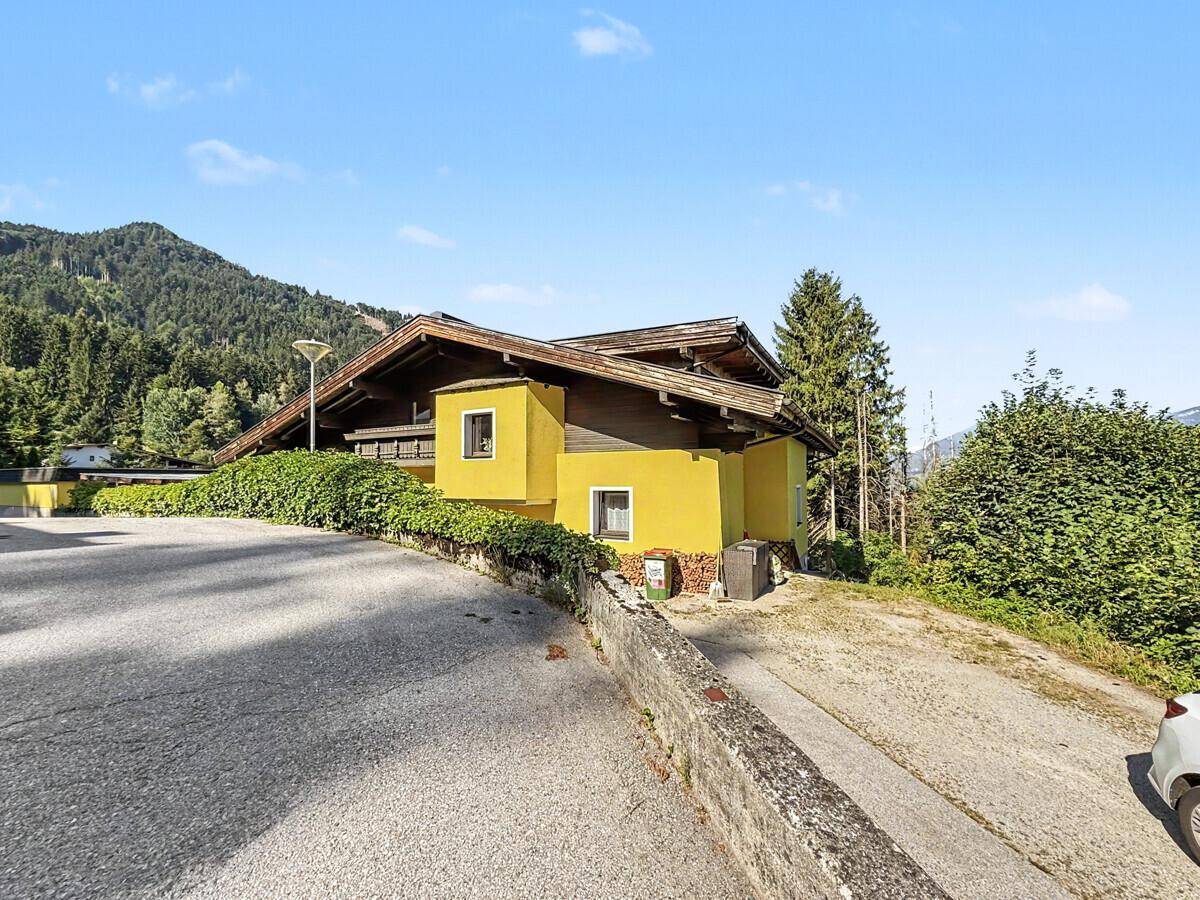 Gelbes Haus mit braunem Dach, umgeben von grünen Hecken und einer Auffahrt.