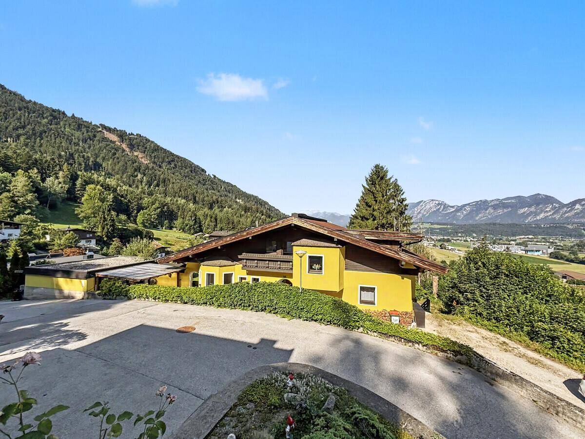 Panoramablick auf das gelbe Haus in einer grünen Berglandschaft unter blauem Himmel.