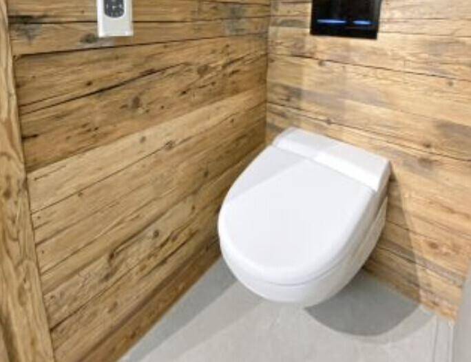 Separate Toilette mit moderner Wandmontage und rustikaler Holzverkleidung an den Wänden.