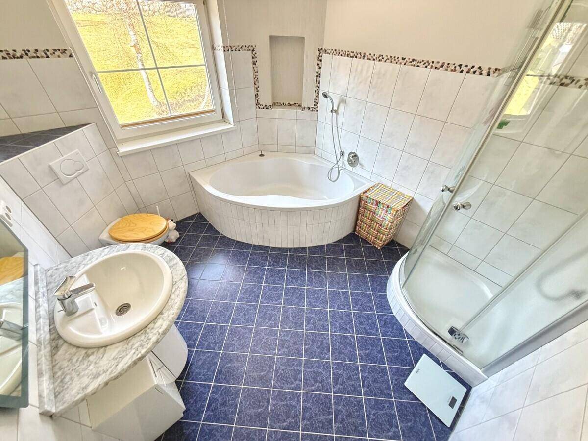 Badezimmer mit blauen Fliesen, Eckbadewanne, separater Dusche und Fenster für Tageslicht.