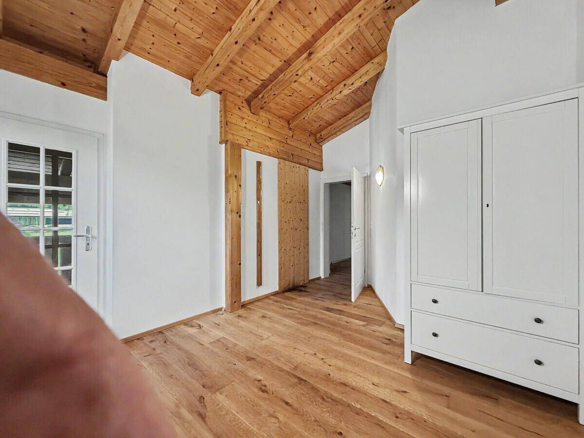 Geräumiges Schlafzimmer mit Holzbalkendecke, Holzboden und Zugang zu einem Balkon.