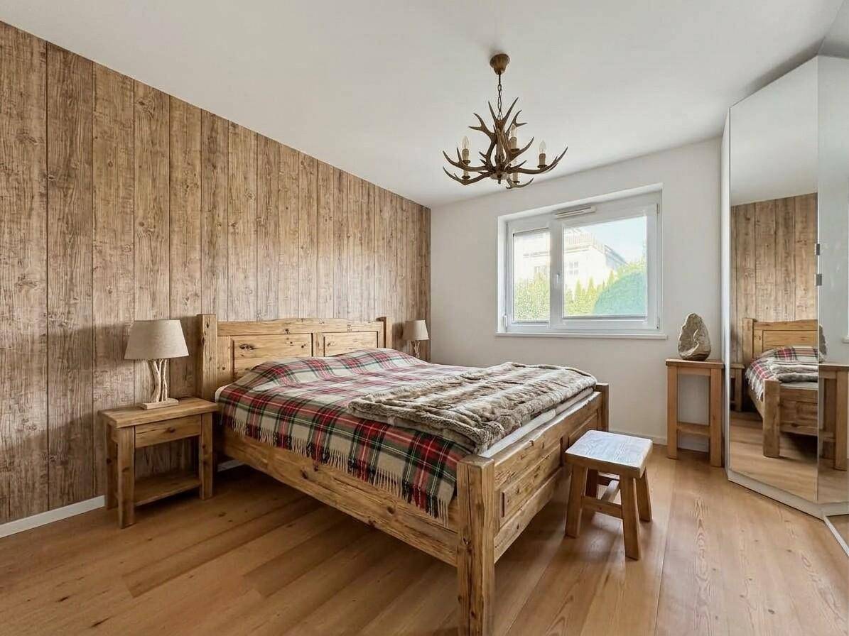 Gemütliches Schlafzimmer im alpinen Stil mit Holzwand, Holzbett und Hirschgeweih-Kronleuchter.