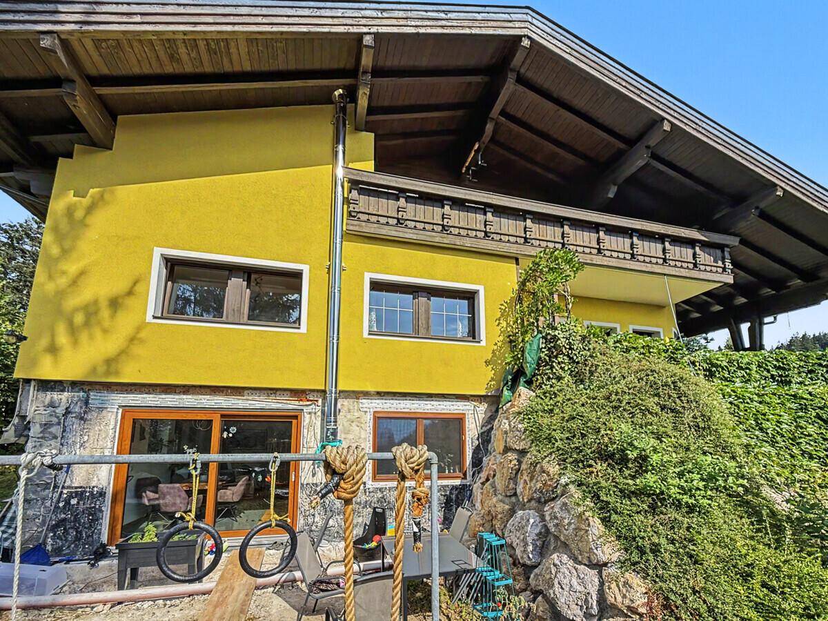 Hausfassade in leuchtendem Gelb mit Holzbalkonen und einer Natursteinmauer.