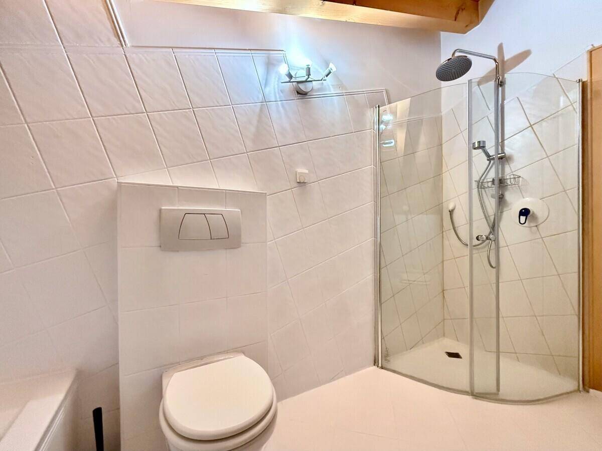 Duschkabine mit Glasabtrennung und wandhängender Toilette in einem gefliesten Badezimmer.