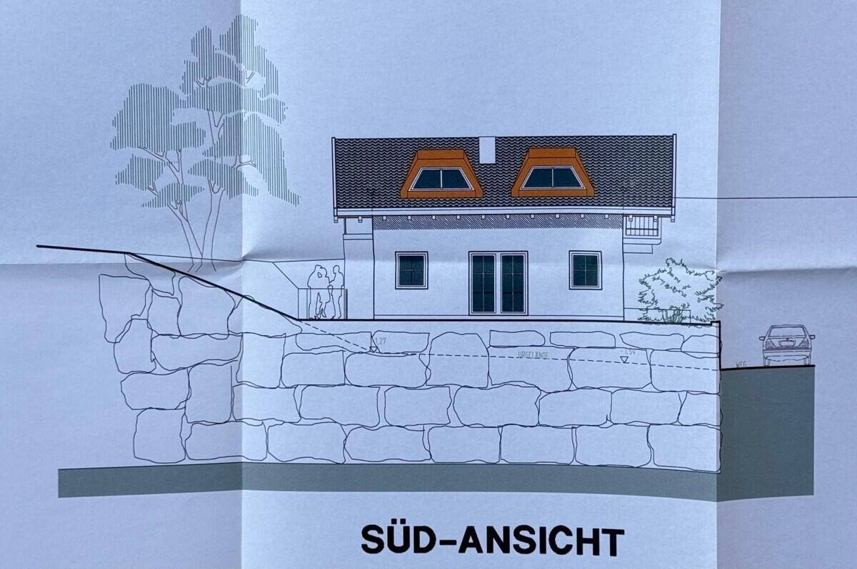 Südansicht des Hauses mit Dachgauben und einer Natursteinmauer im Vordergrund.