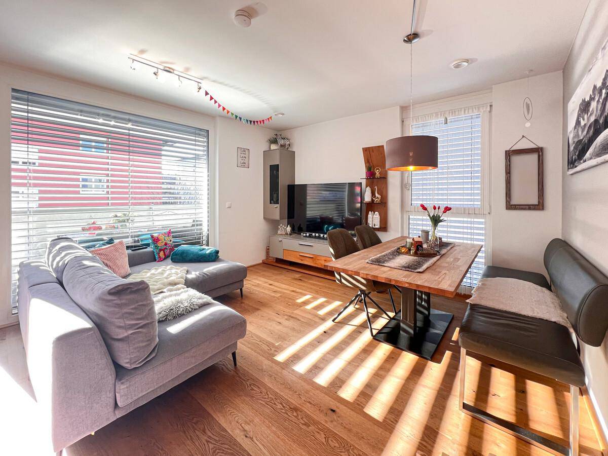 Lichtdurchfluteter Wohnbereich mit bequemer Couch, Esstisch und Zugang zum Balkon.