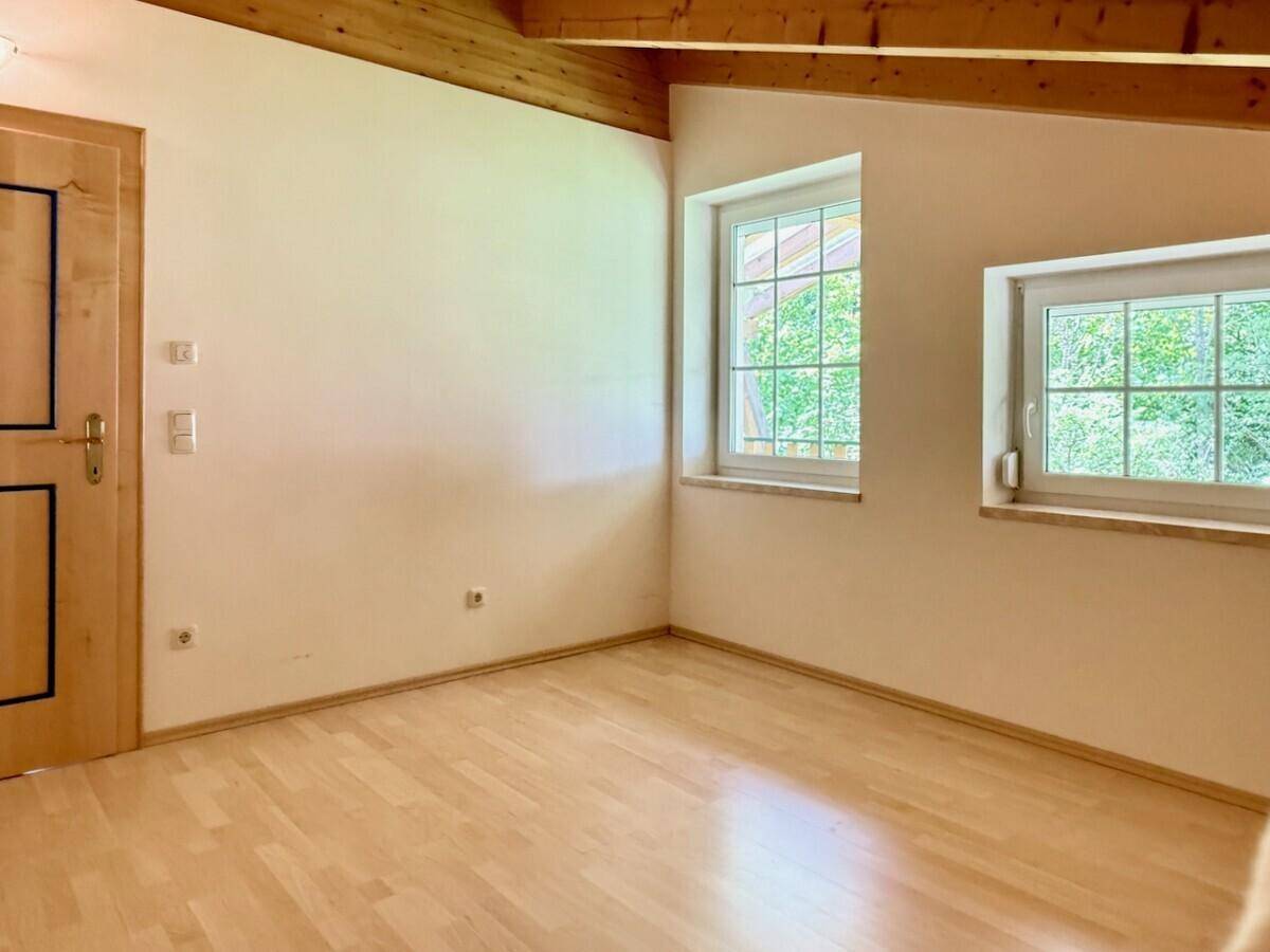 Ecke eines Schlafzimmers mit Holztür, Parkettboden und Fenstern mit Blick ins Grüne.