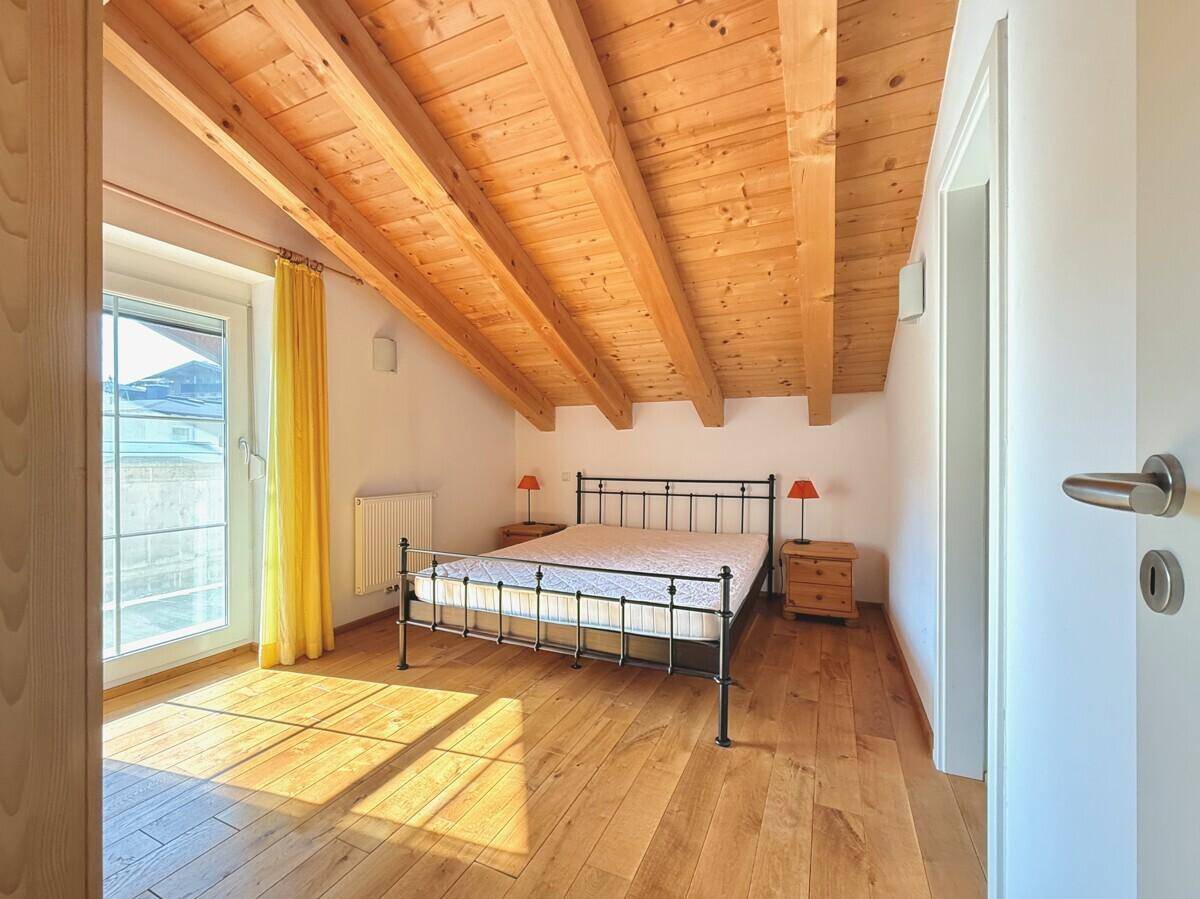 Schlafzimmer im Dachgeschoss mit Holzbalken, Holzboden und direktem Balkonzugang.