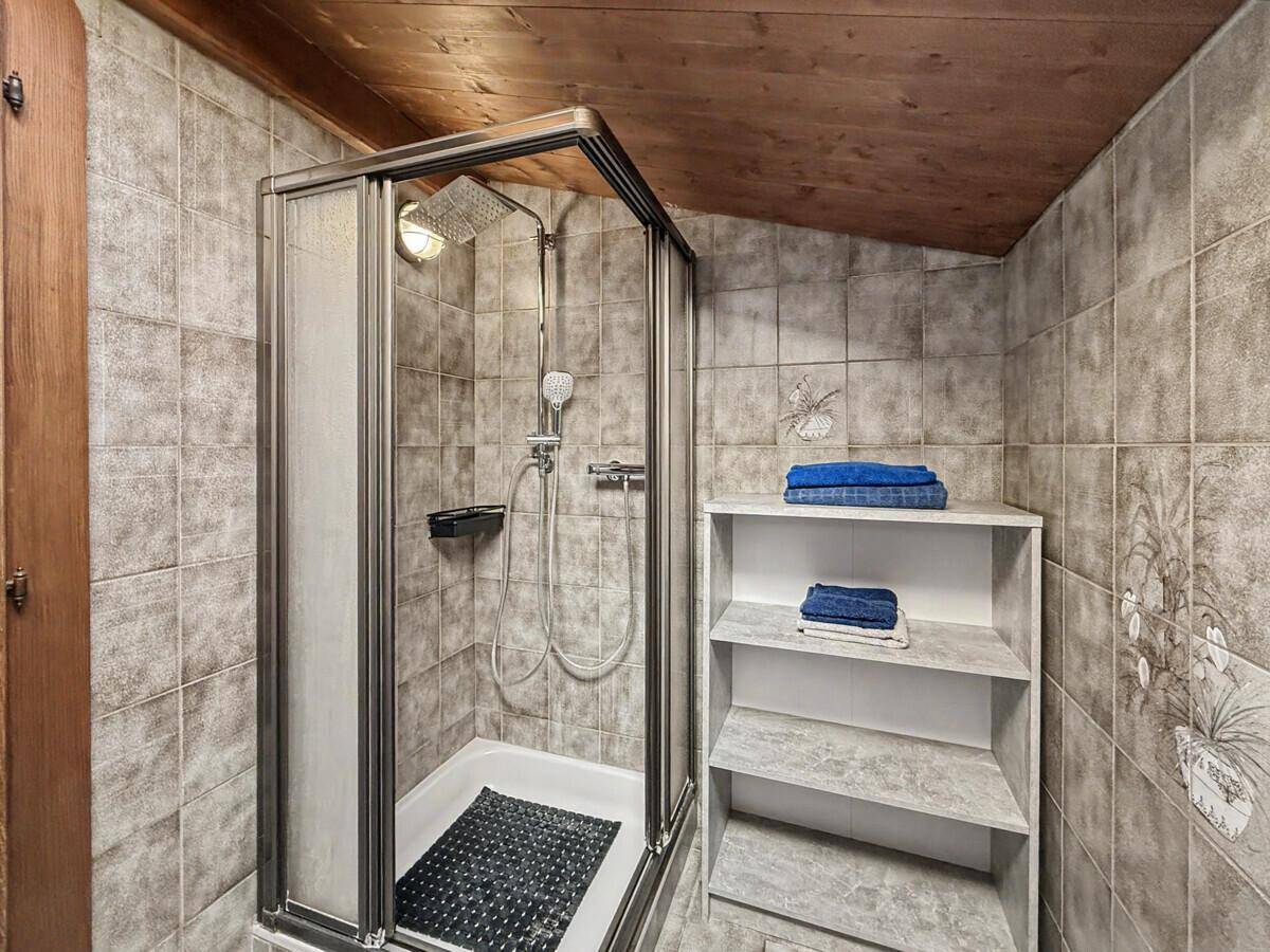 Duschbereich im Badezimmer mit Fliesenwänden und charakteristischer Holzdecke.