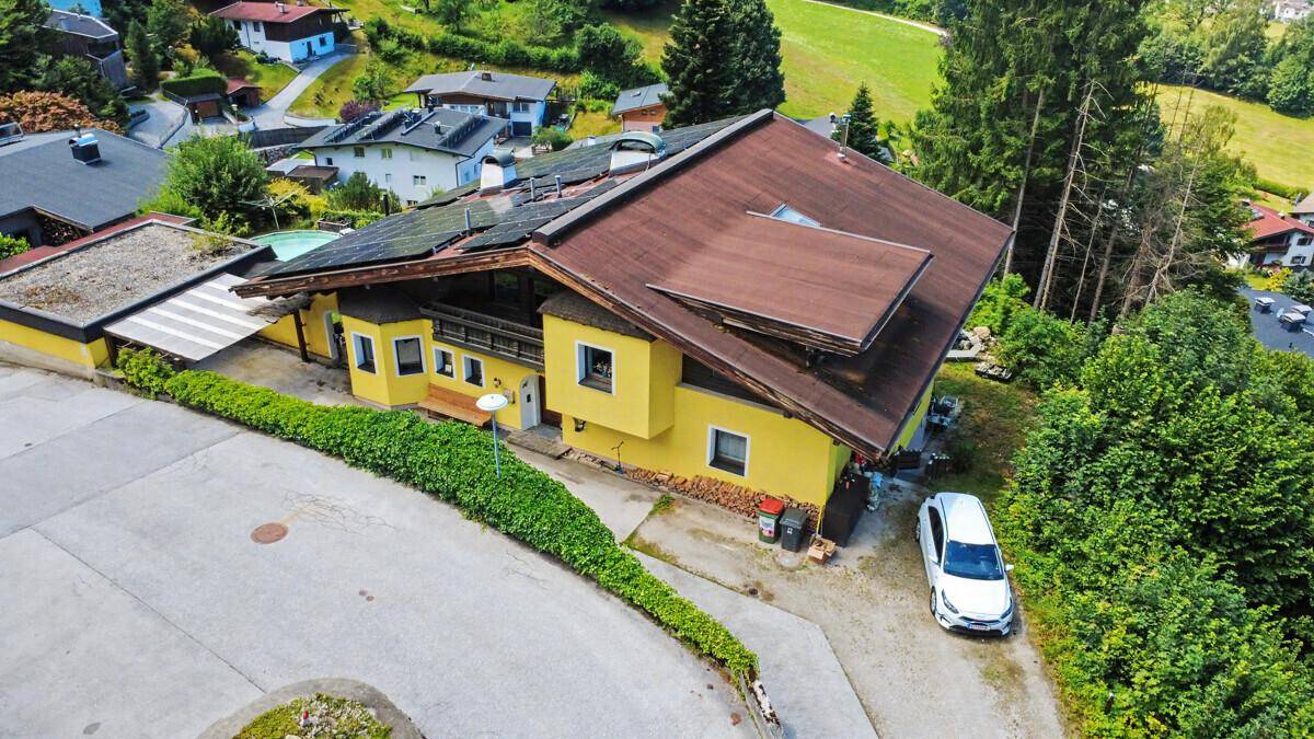 Luftaufnahme des gelben Hauses mit Solaranlage, Auffahrt und einem geparkten Auto.