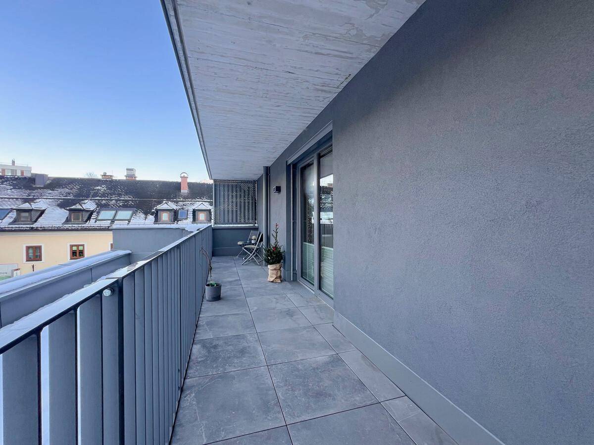 Langer Balkon mit Fliesenboden und Blick auf die Stadt und die Berge.