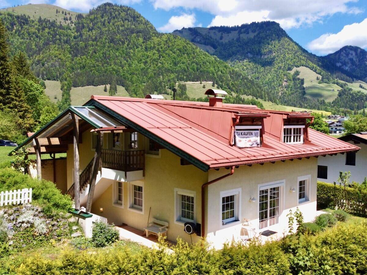 Charmantes Haus mit rotem Dach und Balkon in malerischer Berglandschaft.