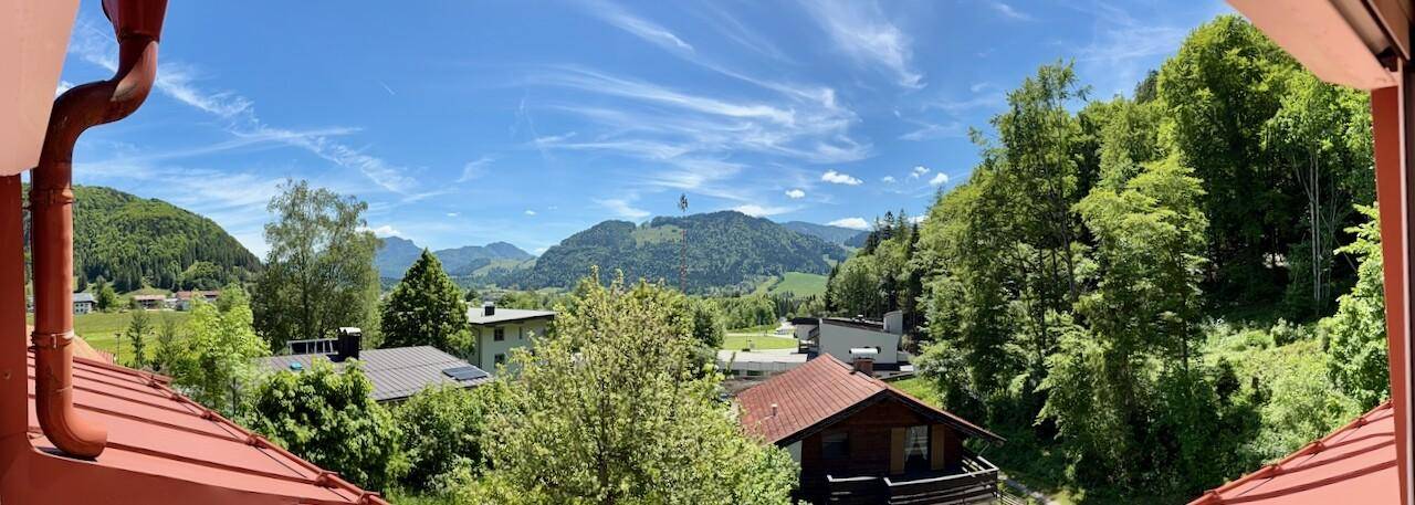 Panoramablick auf die umliegende Berglandschaft mit grünen Hügeln und Häusern unter blauem Himmel.