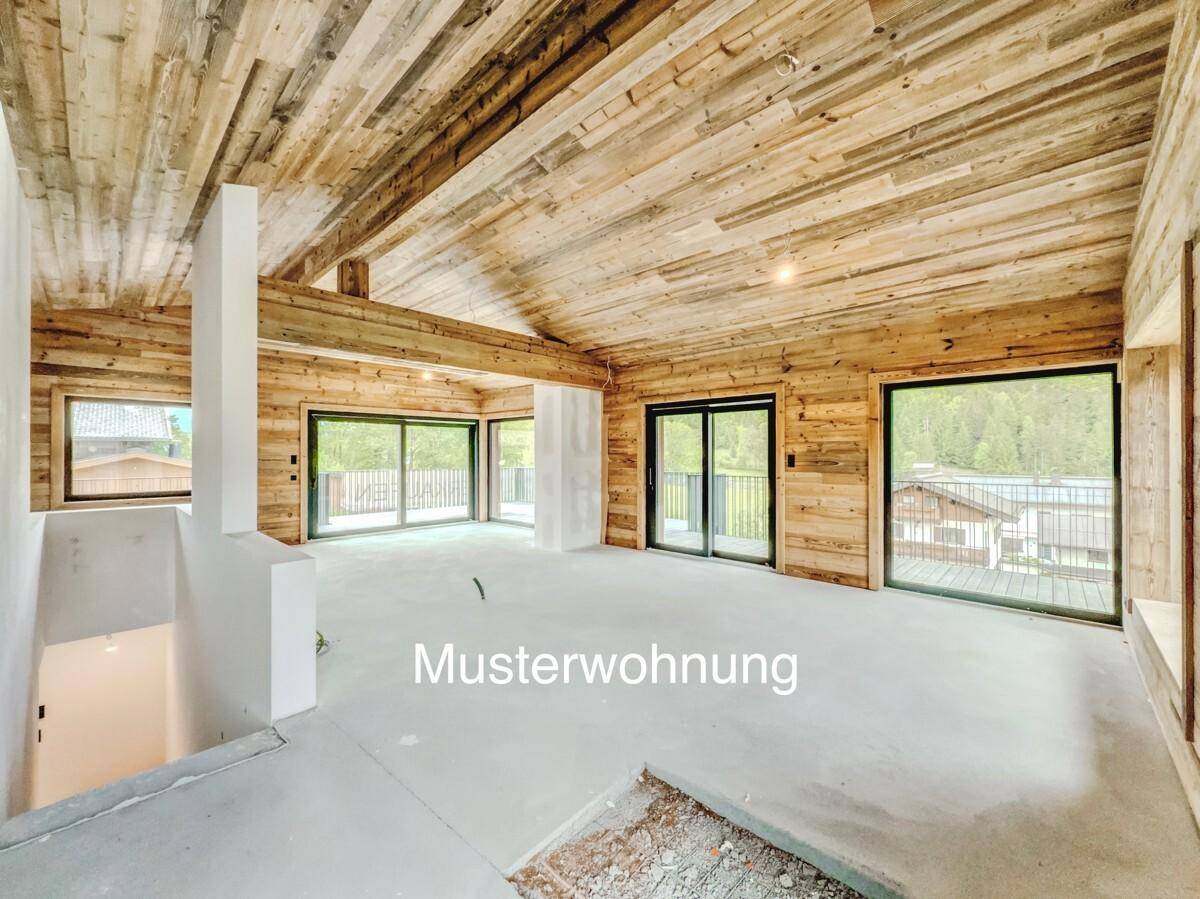 Geräumiger Innenraum einer Musterwohnung im Bau mit Holzbalkendecke und großen Fenstern.