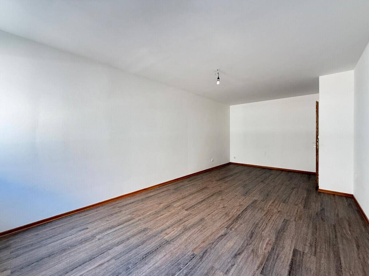 Helles Zimmer mit Laminatboden und weißen Wänden, bereit zur individuellen Gestaltung.