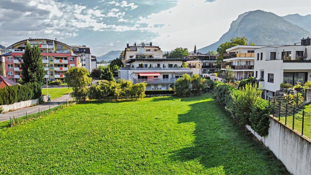 Großzügige Grünfläche umgeben von Wohngebäuden und Bergen unter einem bewölkten Himmel.
