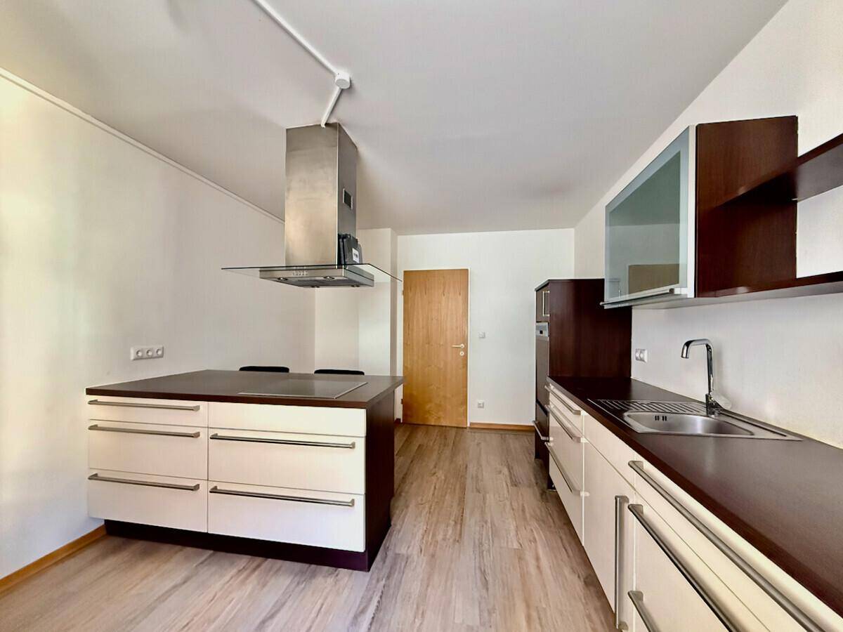 Moderne Küche mit Kochinsel, Dunstabzugshaube und integrierten Geräten in dunklem Holzdesign.