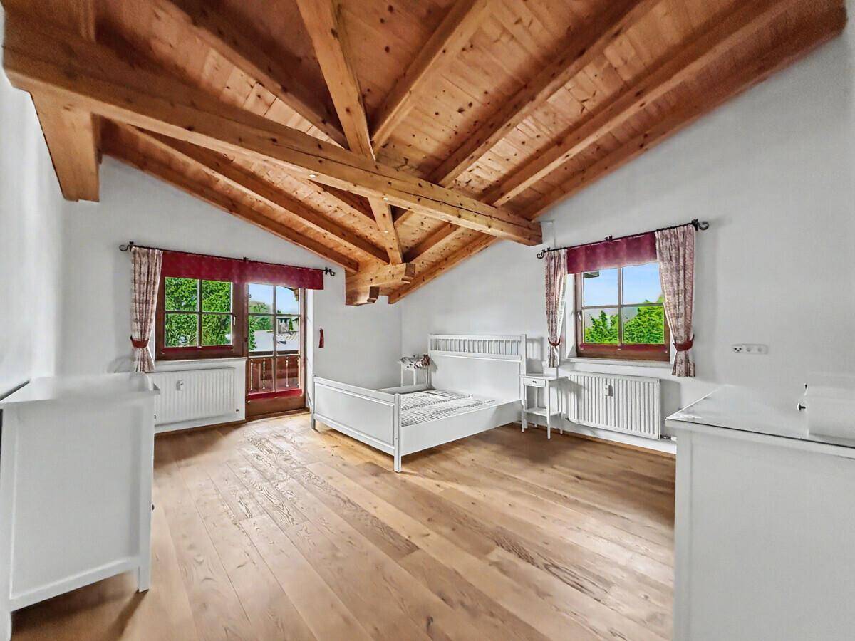 Gemütliches Schlafzimmer mit Holzbalkendecke, Holzboden und Balkonzugang mit grüner Aussicht.
