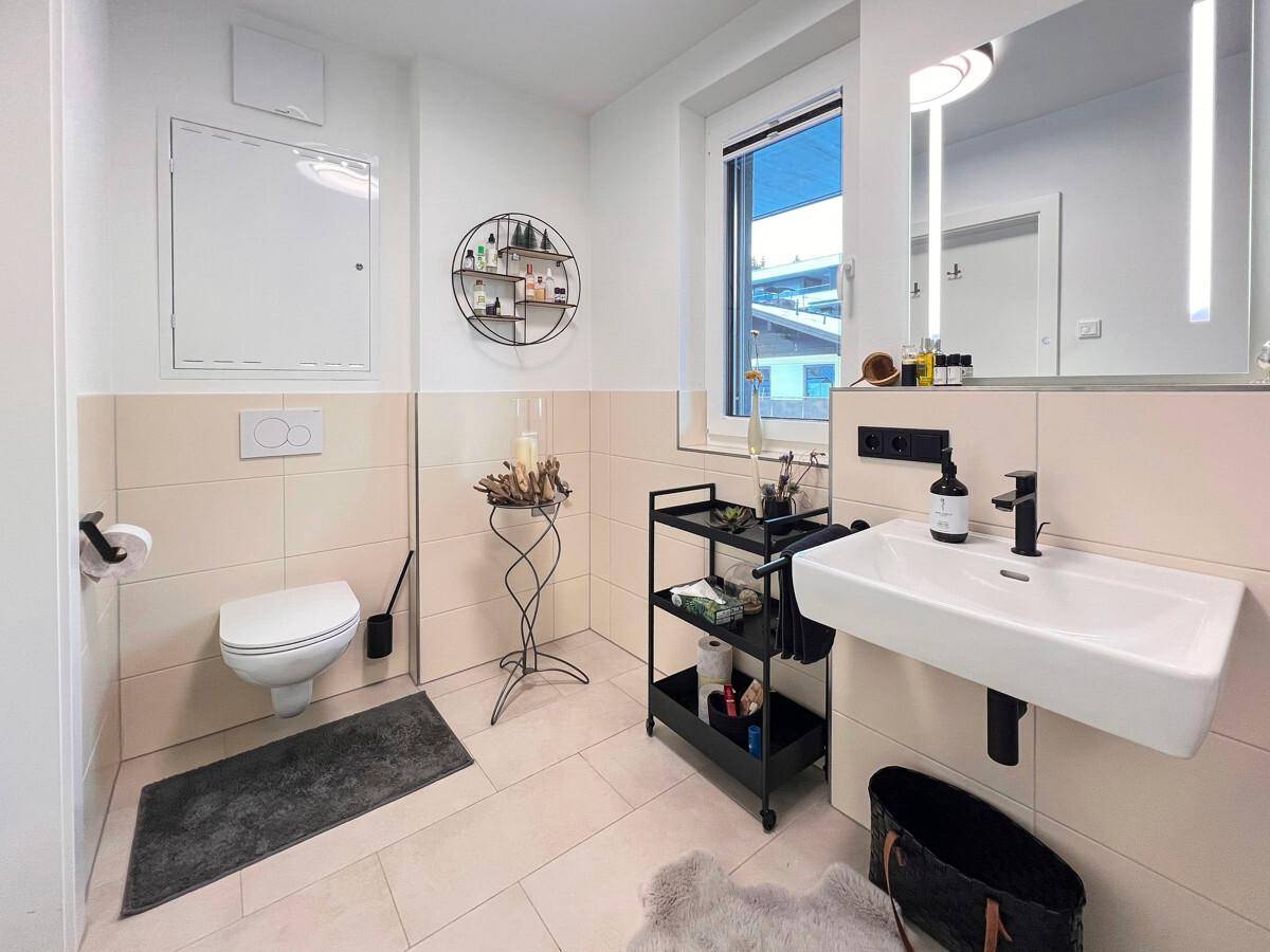 Modernes Badezimmer mit Waschtisch, Spiegel und Wand-WC, hell gefliest.
