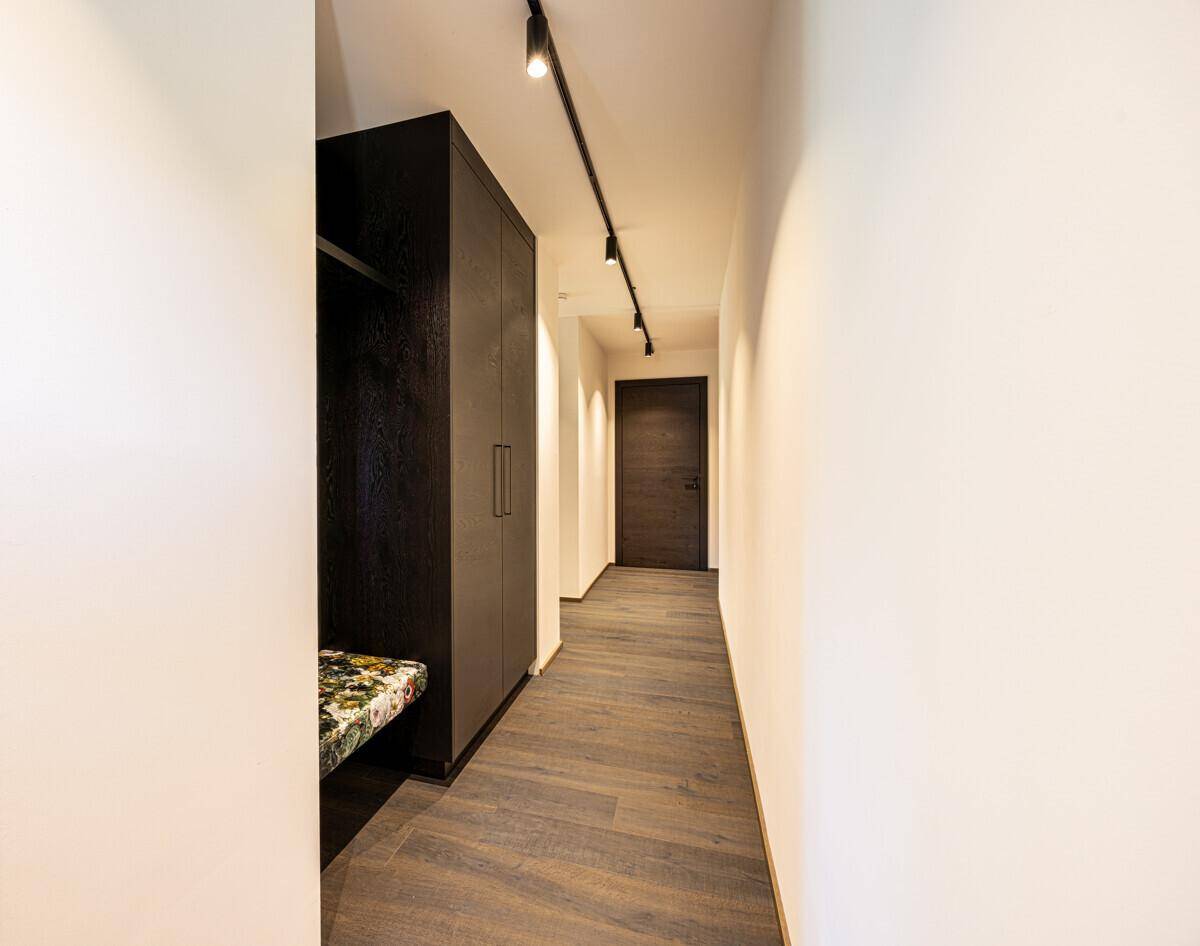Heller Flur mit integriertem Kleiderschrank und dunklem Holzboden, der zu weiteren Räumen führt.