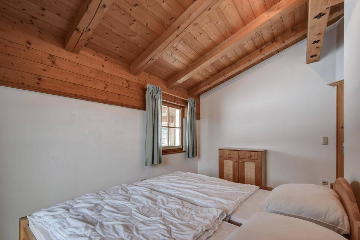 Helles Schlafzimmer mit schräger Holzbalkendecke, Parkettboden und Fenster mit Bergblick.