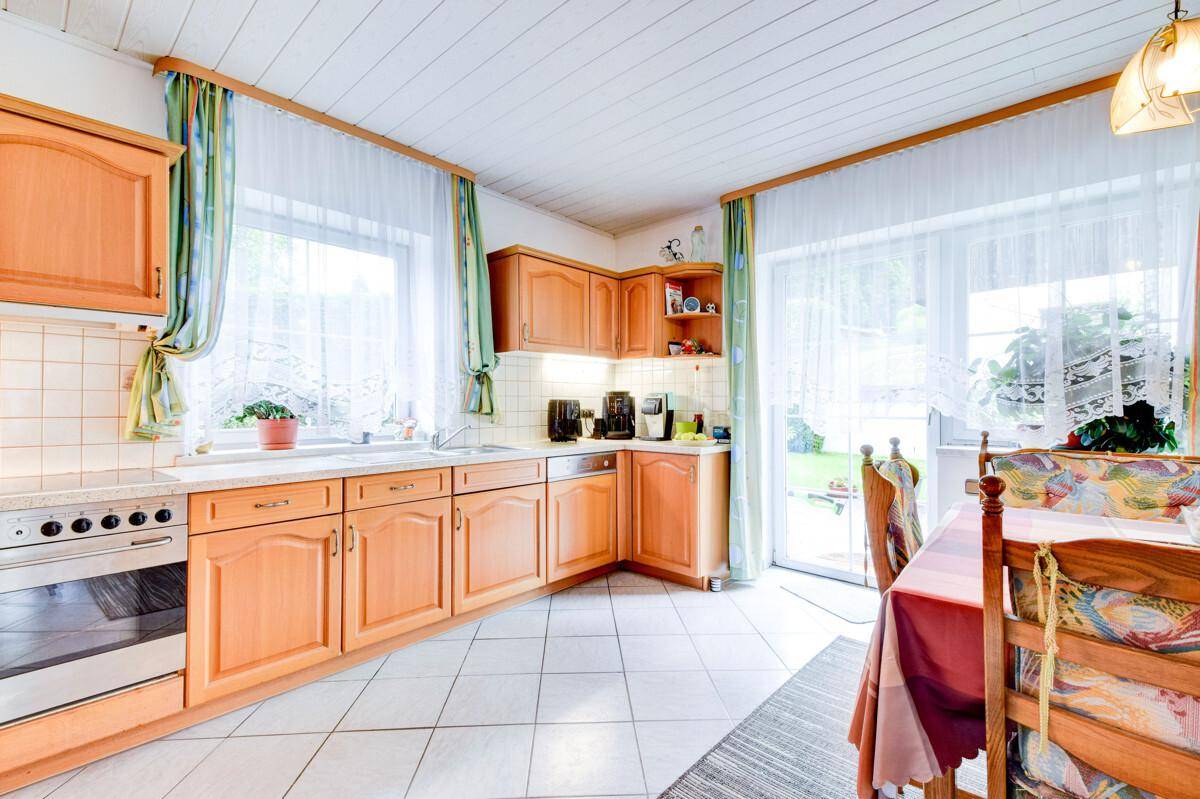 Gemütliche Küche mit hellen Holzschränken, weißen Fliesen und einem Essbereich am Fenster.
