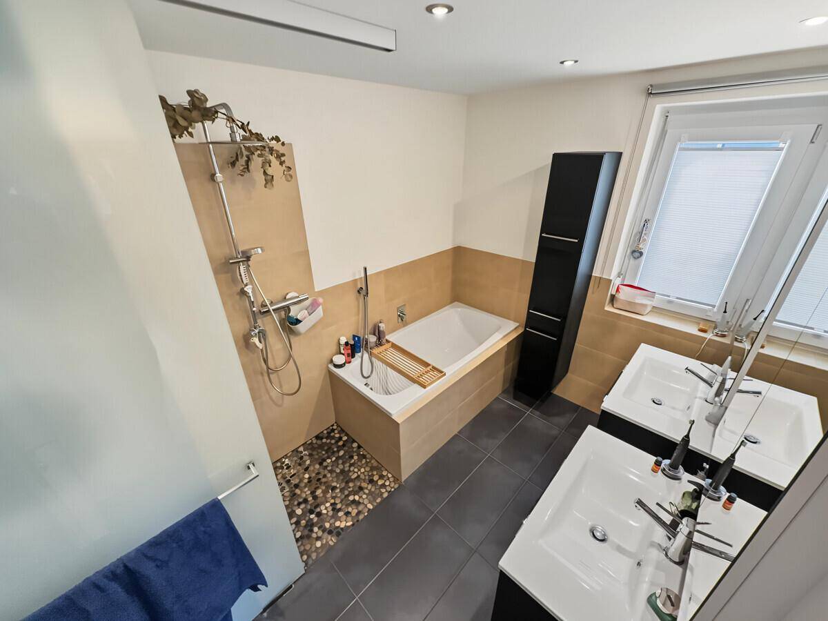Modernes Badezimmer mit Doppelwaschbecken, Badewanne und begehbarer Dusche mit Kieselsteinen.