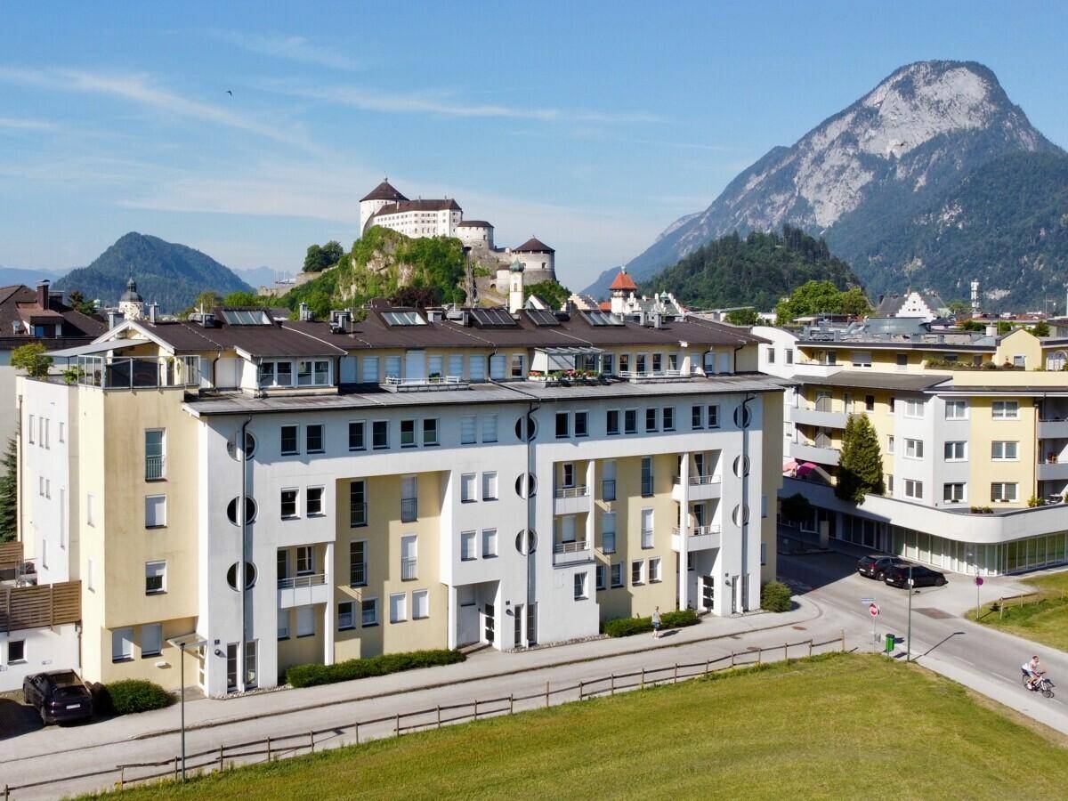 Mehrfamilienhaus mit moderner Architektur und Blick auf die umliegende Berglandschaft und Burg.