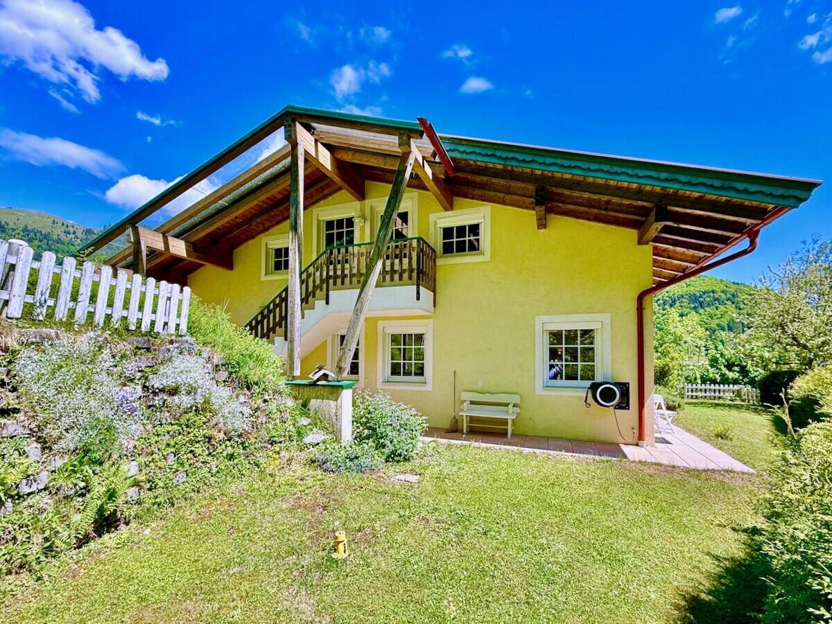 Hausfassade mit Gartenbereich, Rasenfläche und Blick auf die Berge.