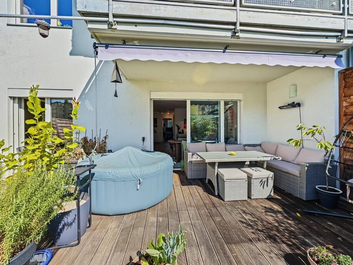 Geräumige Holzterrasse mit Lounge-Möbeln, Sonnenschutz und aufblasbarem Whirlpool.