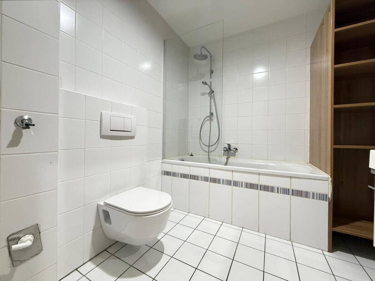 Badezimmer mit Badewanne, Duschvorrichtung, wandhängendem WC und weißen Fliesen.