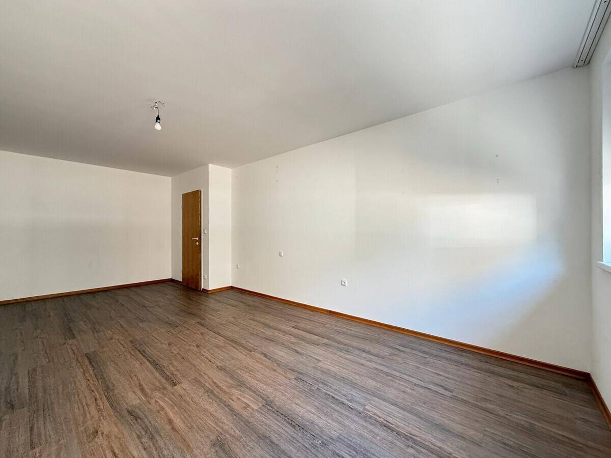 Leeres Zimmer mit Laminatboden, weißen Wänden und einer Holztür.