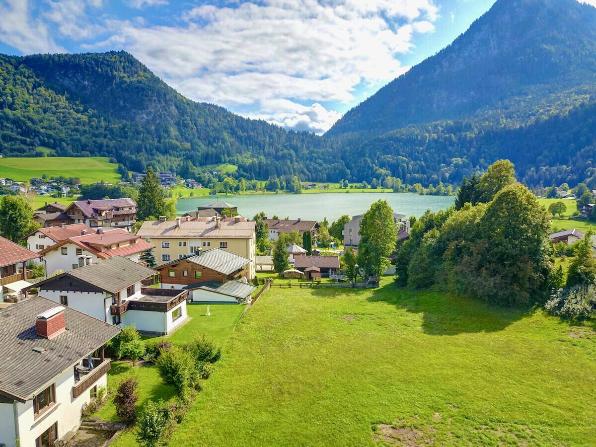 Malerische Landschaft mit einem See, umgeben von grünen Bergen und ländlicher Bebauung.