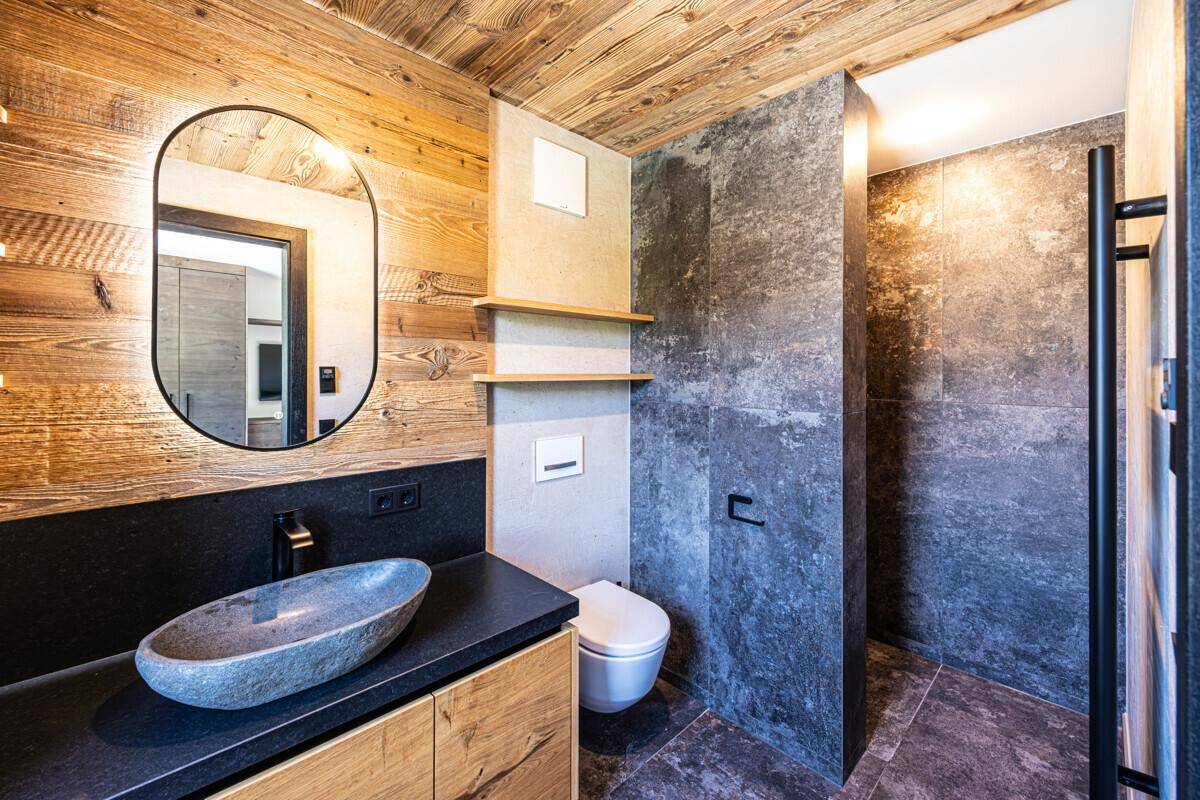 Modernes Badezimmer mit Steinswaschbecken, dunklen Fliesen, Holzdecke und begehbarer Dusche.