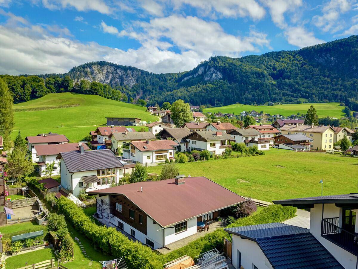 Luftaufnahme einer ländlichen Siedlung mit grünen Wiesen und Bergen im Hintergrund.