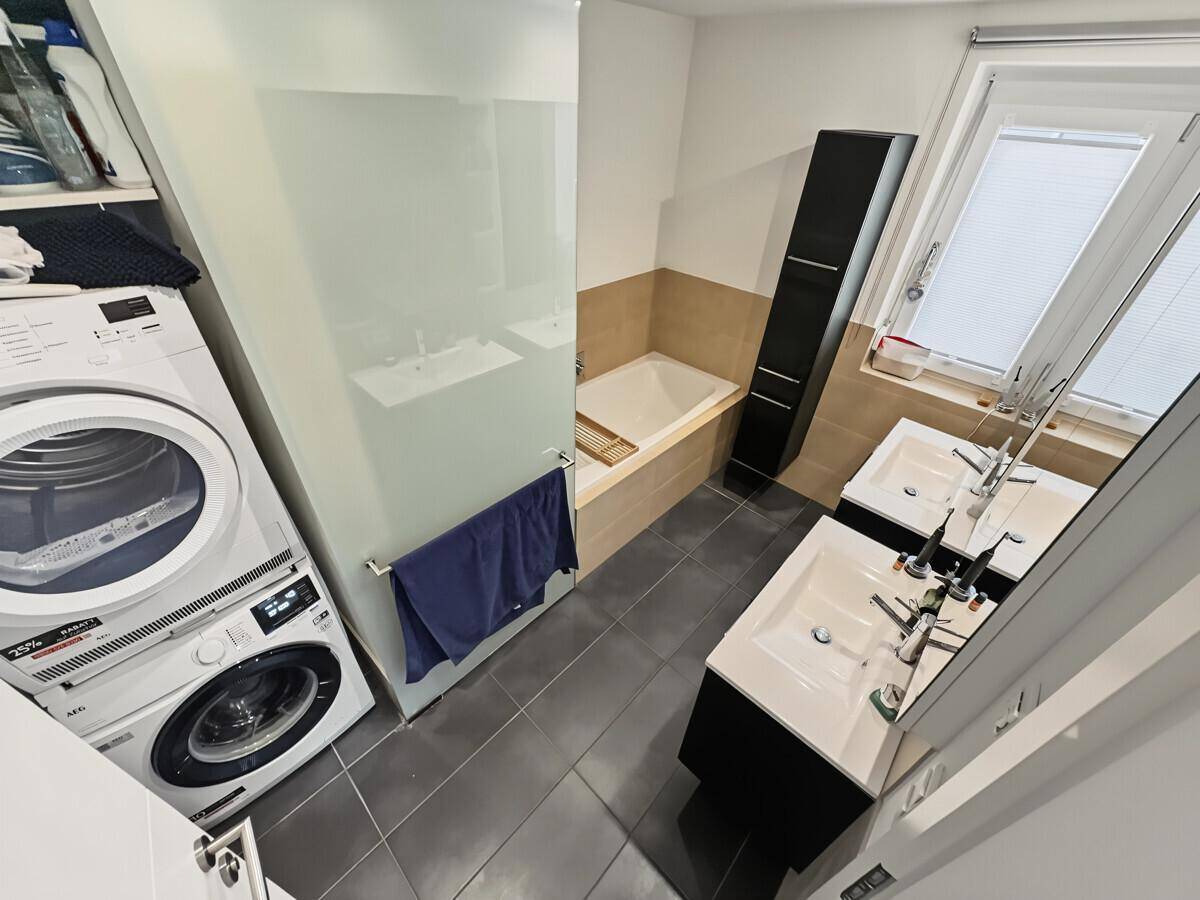 Badezimmer mit Waschmaschine, Trockner, Badewanne und Doppelwaschbecken.