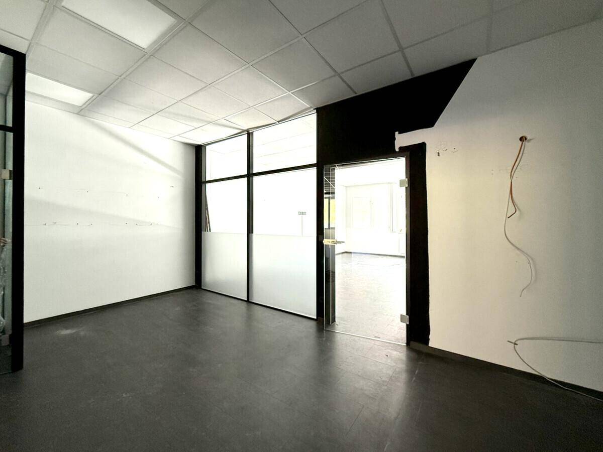 Leerer Büroraum mit großen Fenstern und dunklem Boden, ideal für flexible Arbeitsplatzgestaltung.