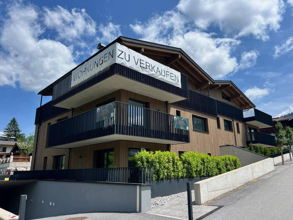 Neues Wohngebäude mit Holzfassade und schwarzen Balkongeländern an einem hellen, sonnigen Tag.