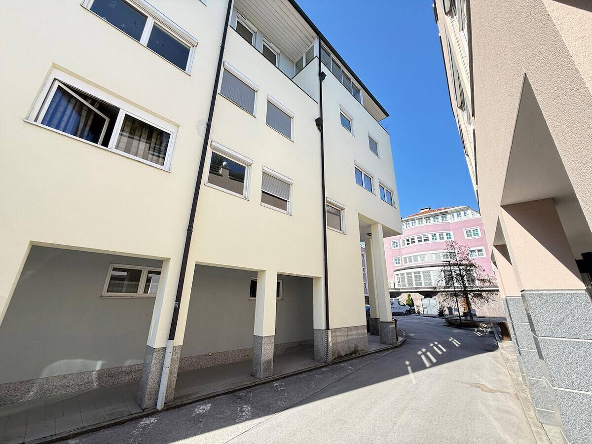 Seitenansicht eines modernen Gebäudes mit heller Fassade und überdachten Parkplätzen im Erdgeschoss.