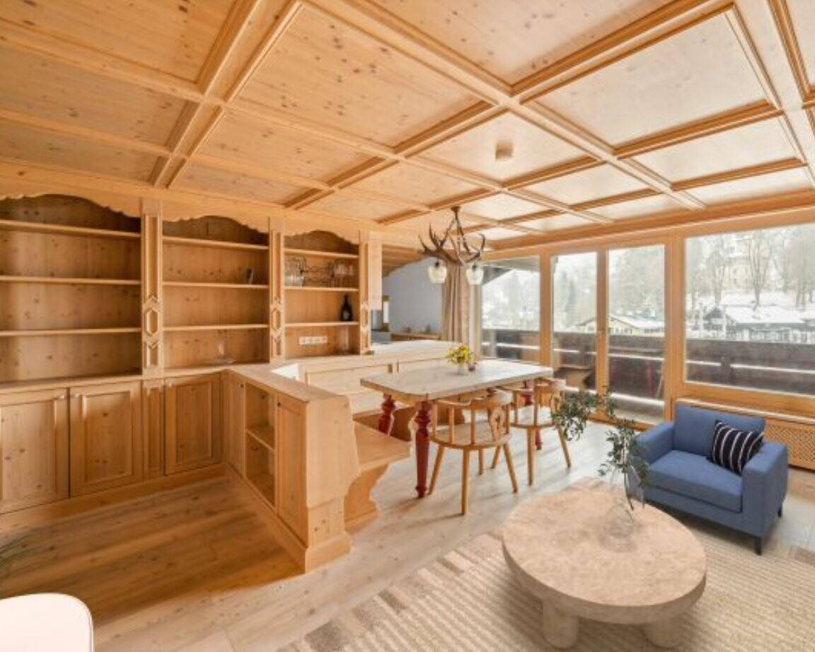 Gemütlicher Wohn-Essbereich im alpinen Stil mit Holztäfelung, Einbauschränken und Blick auf die verschneite Landschaft.