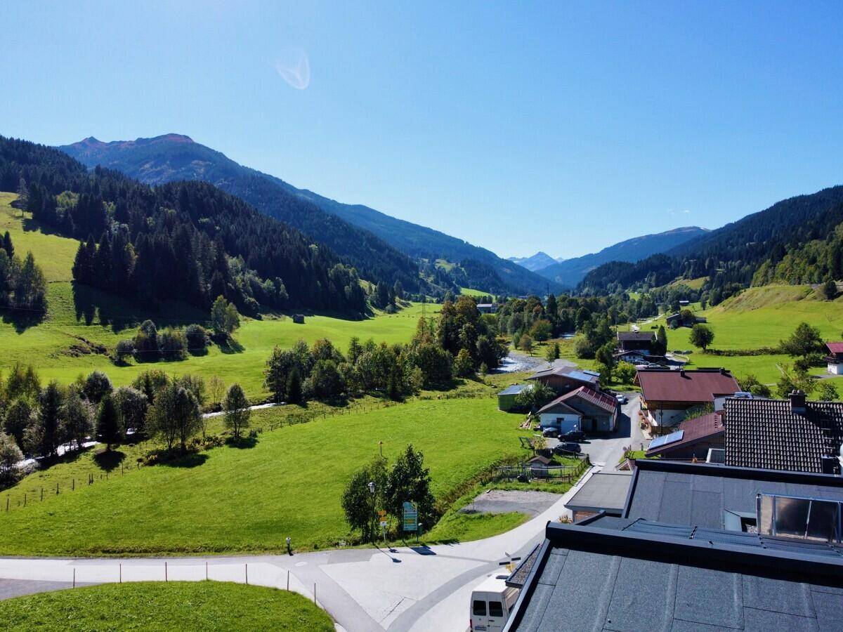 Weiter Blick über das Tal mit bewaldeten Bergen und kleinen Siedlungen unter blauem Himmel.