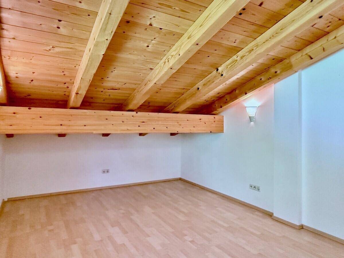Helles Schlafzimmer im Dachgeschoss mit Holzbalkendecke und Parkettboden.