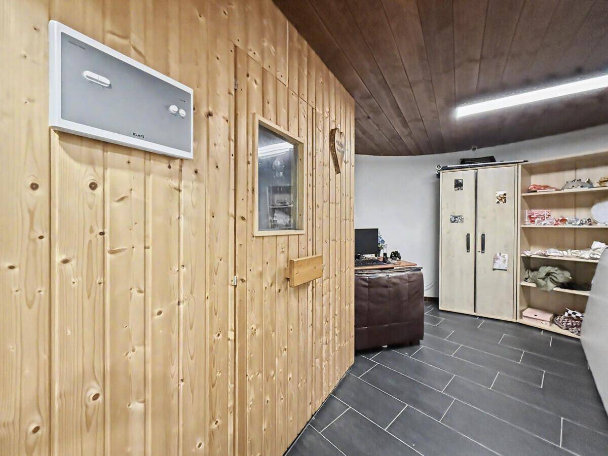 Flur mit dunklem Fliesenboden und Holzwand, mit Blick auf eine angrenzende Sauna.