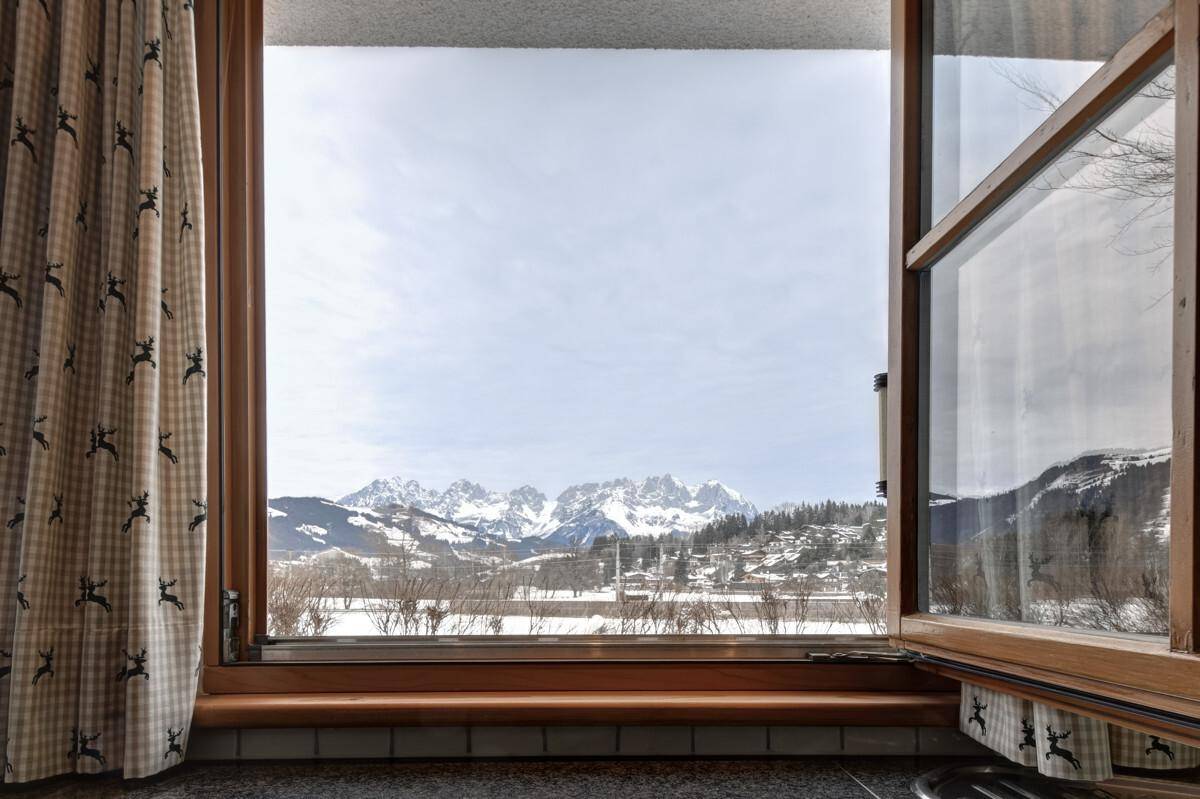 Fensterblick auf die weite, verschneite Landschaft und die beeindruckende Bergkette am Horizont.