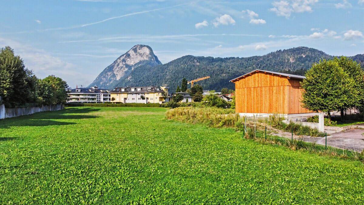 Weitläufige Grünfläche mit umliegenden Gebäuden und beeindruckendem Bergblick im Hintergrund.