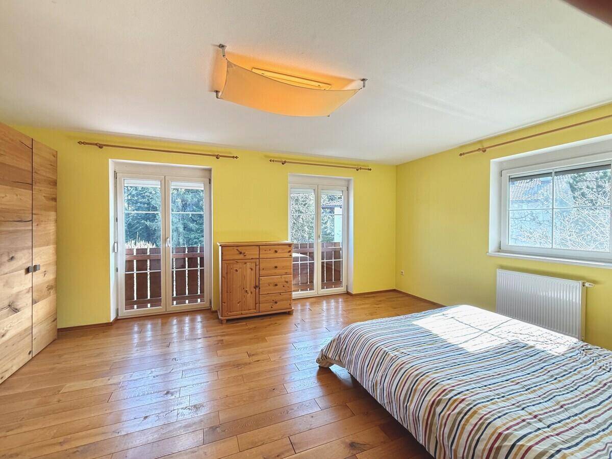 Schlafzimmer mit gelben Wänden, Holzboden und zwei Türen, die zum Balkon führen.