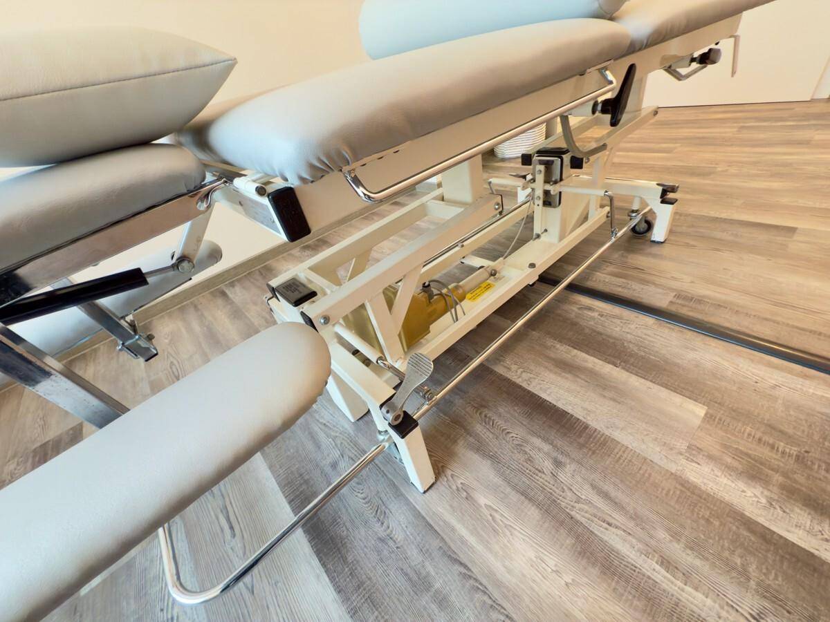 Detailansicht einer modernen, höhenverstellbaren Therapieliege mit Rollen in einem Behandlungsraum.