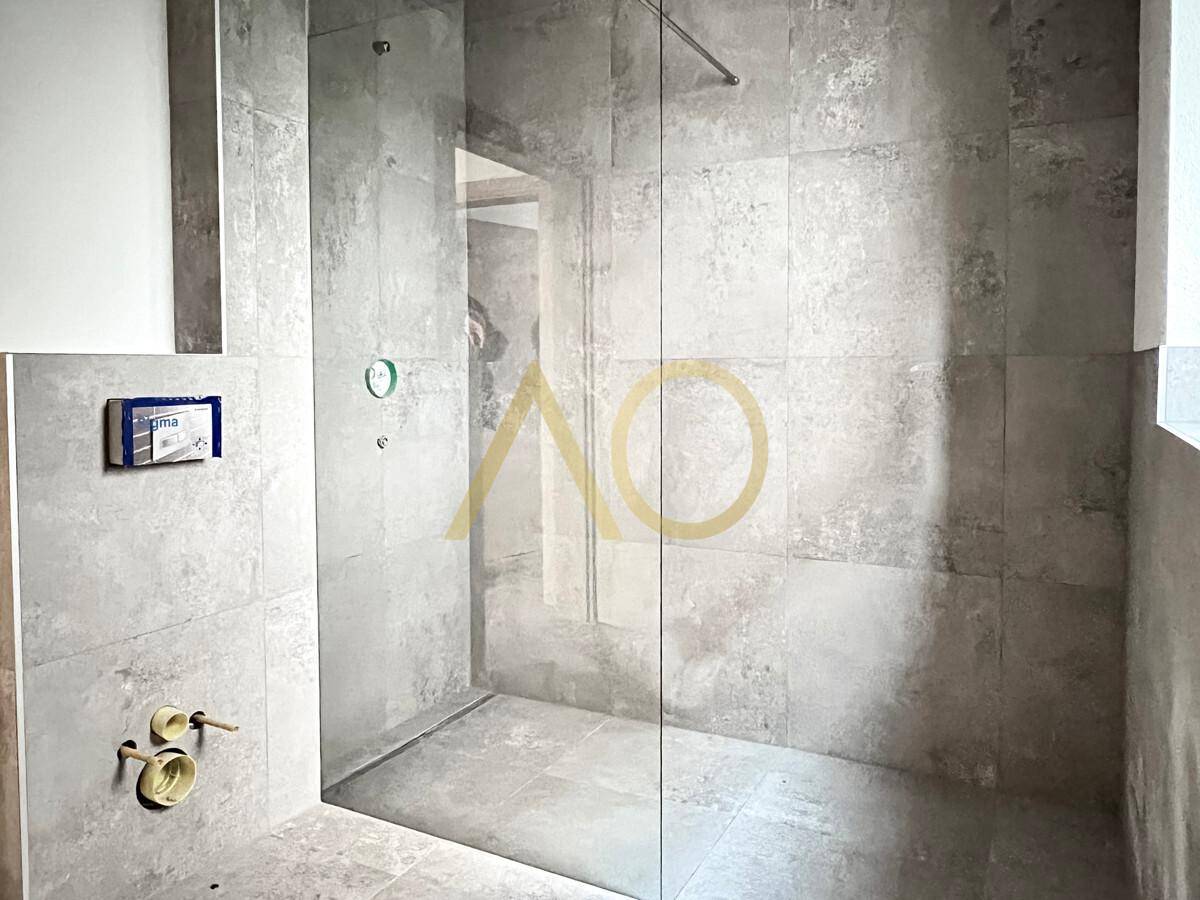 Moderne Dusche mit grauen Fliesen, Glasabtrennung und Duscharmaturen.