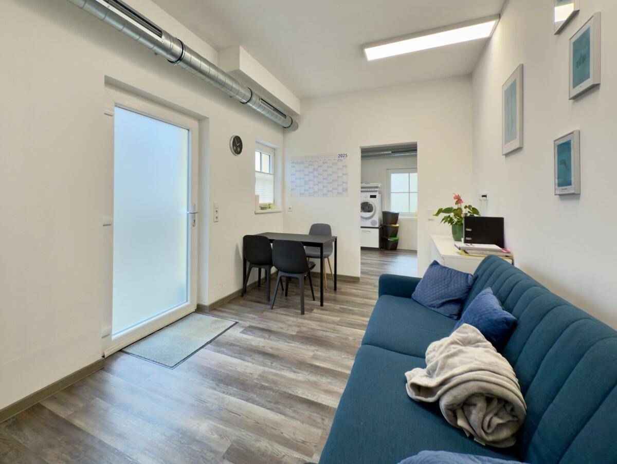 Gemütlicher Pausenraum mit Sofa, Esstisch und Zugang zu einem weiteren Bereich.